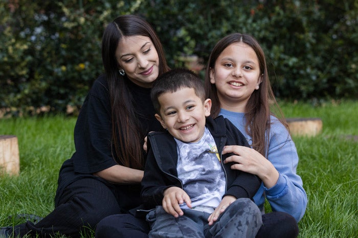 A mother, son and daughter sitting on some grass smiling at the camera
