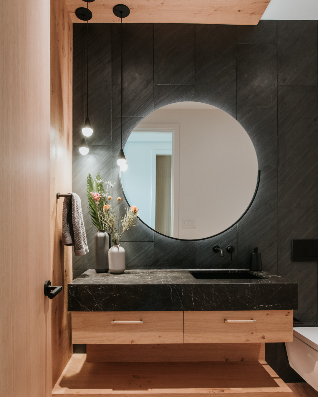 A bathroom with a round mirror and a black countertop - wood veneer - natural oak