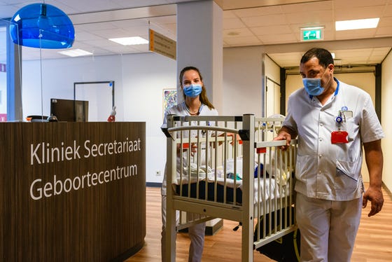 Pasgeboren baby wordt door twee zorgverleners in een bedje op wielen vervoerd in het WKZ.