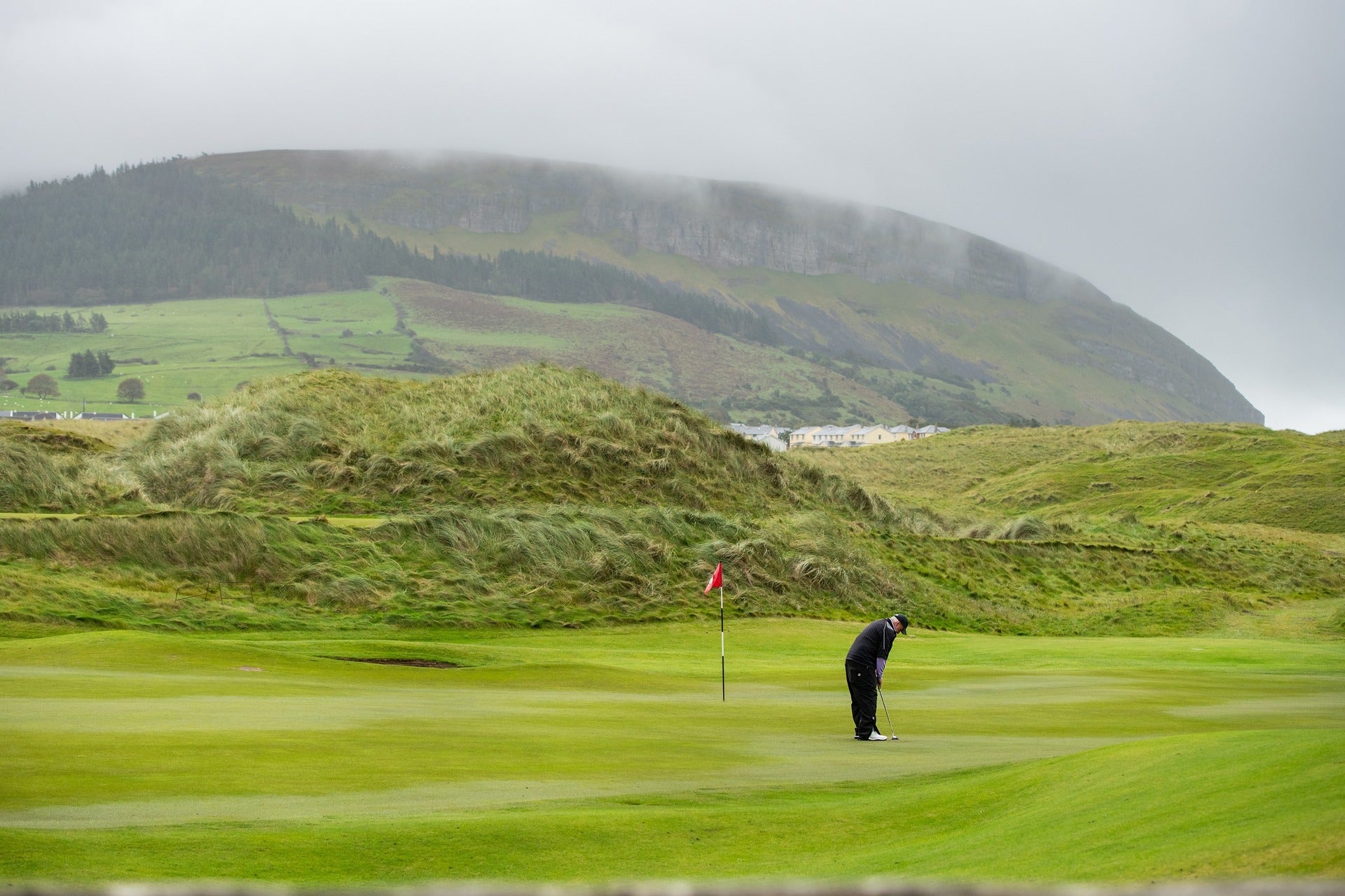 Lone golfer putting on a links green with misty hills and coastal scenery in the background