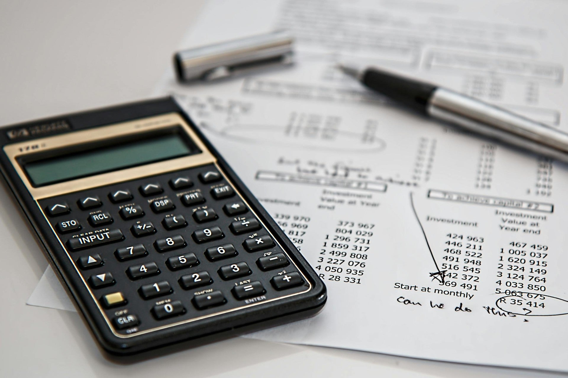 Financial calculator placed on printed investment spreadsheets with a pen