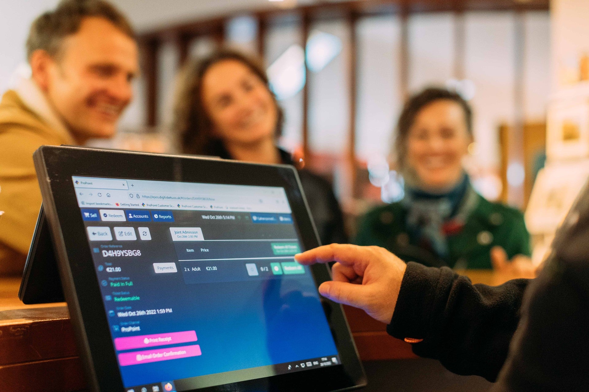 Staff member operating a touchscreen point-of-sale and ticketing system, with customers visible in the background