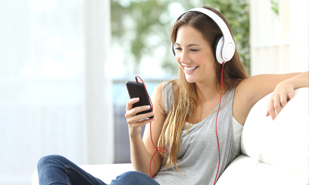 Žena so slúchadlami na ušiach a pozerajúca sa na telefón