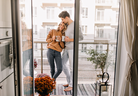 Muž a žena stojaci na balkóne a držiaci šálky kávy