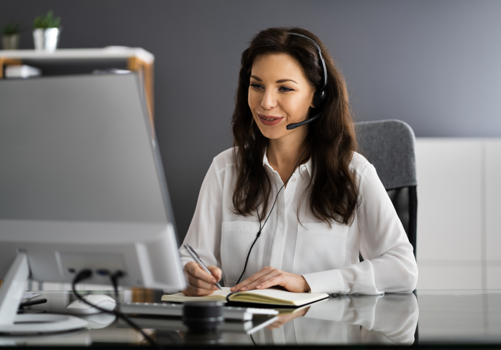 Kobieta nosząca zestaw słuchawkowy i pisząca w notatniku
