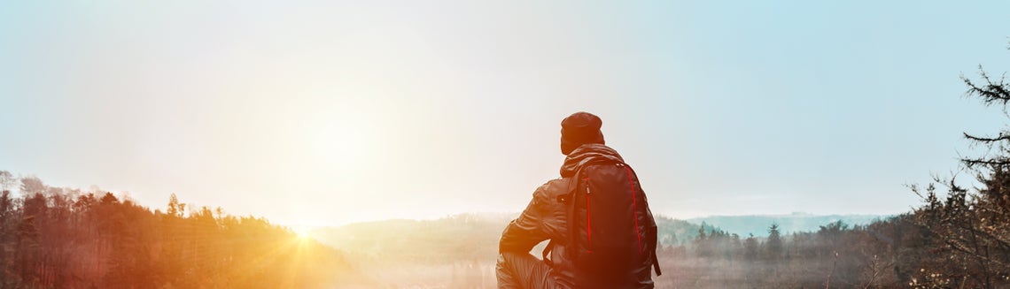 Osoba sedící na skále a dívající se na západ slunce