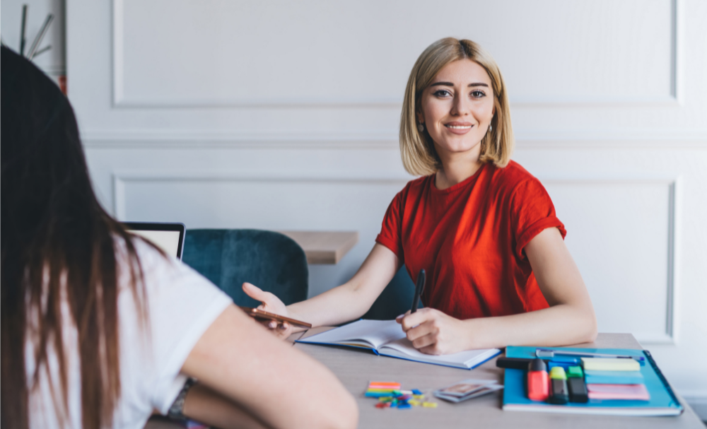 Žena sediaca pri stole so ženou v červenej košeli