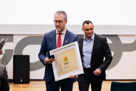 Muž v obleku drží zarámovaný certifikát