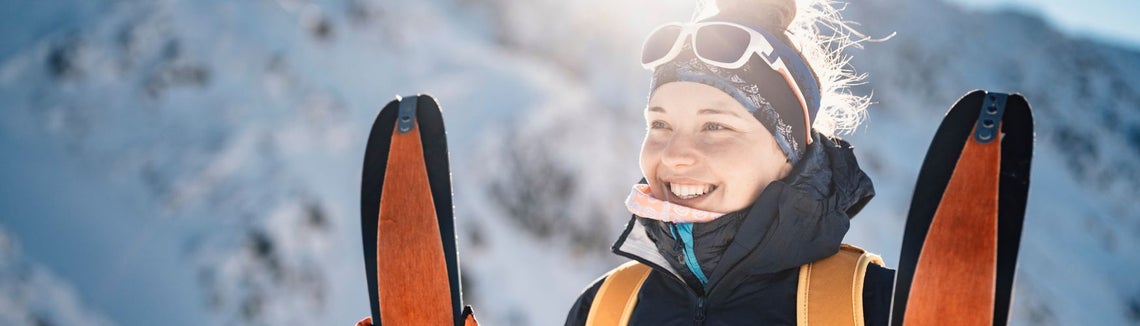 Kobieta w okularach przeciwsłonecznych i kapeluszu trzymająca narty