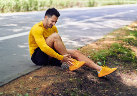 Muž sediaci na okraji cesty a držiaci si topánku