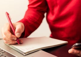 osoba w czerwonym swestrze, która notuje w notatniku czerwonym długopisem