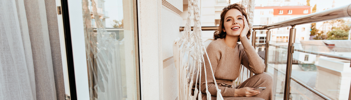 kobieta siedzi zrelaksowana i uśmiechnięta na balkonie