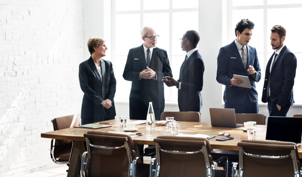Skupina ľudí v oblekoch stojacich okolo stola