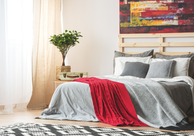 wnętrze mieszkania, sypialnia z łózkiem przykrytym szarą narzutą, czerwony koc, przytulne wnętrze
