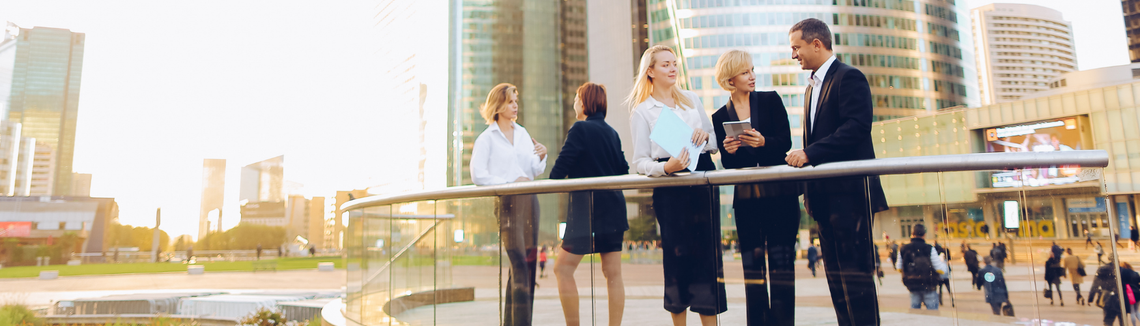 Pracownicy stoją i rozmawiają, w tle budynki biurowe, rozmowy pracowników