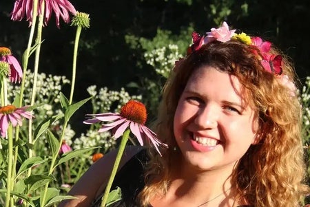 A smiling woman holding a flower, surrounded by flowering plants.