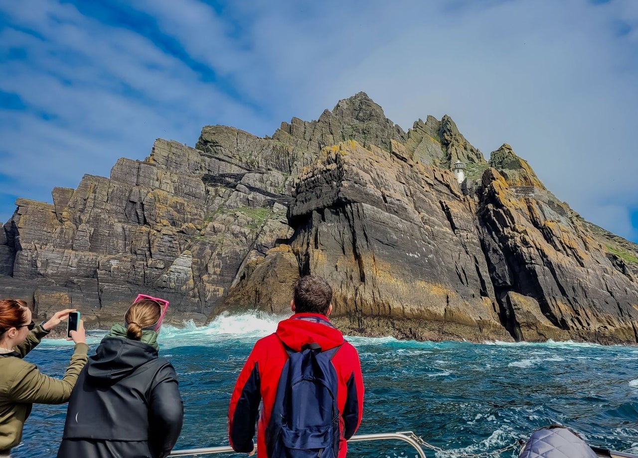 Three passengers on a tour boat taking photos of Little Skellig island