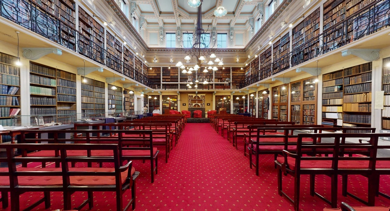 A library with wall to wall books and shelves with tables and chairs in a row 