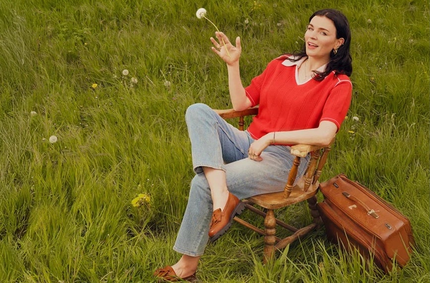 A woman seated in a wooden chair on grass