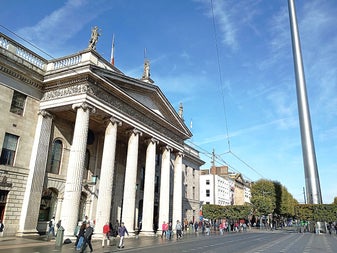 The General Post Office in Dublin with people walking nearby and the Spire in the background