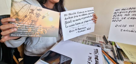 A lady holding two cards with Irish calligraphy on them