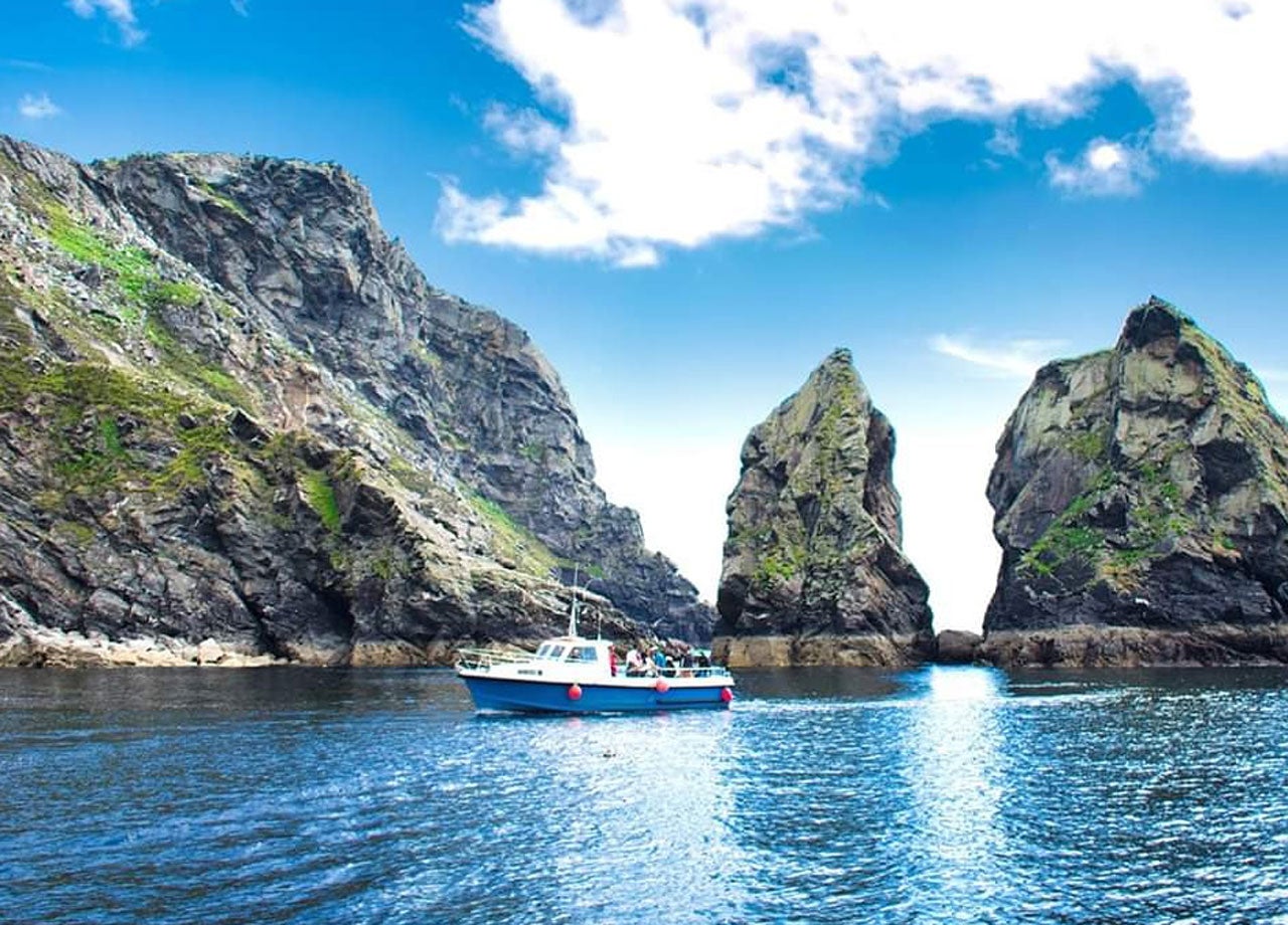 A blue boat out on the water with the sea cliffs in the background