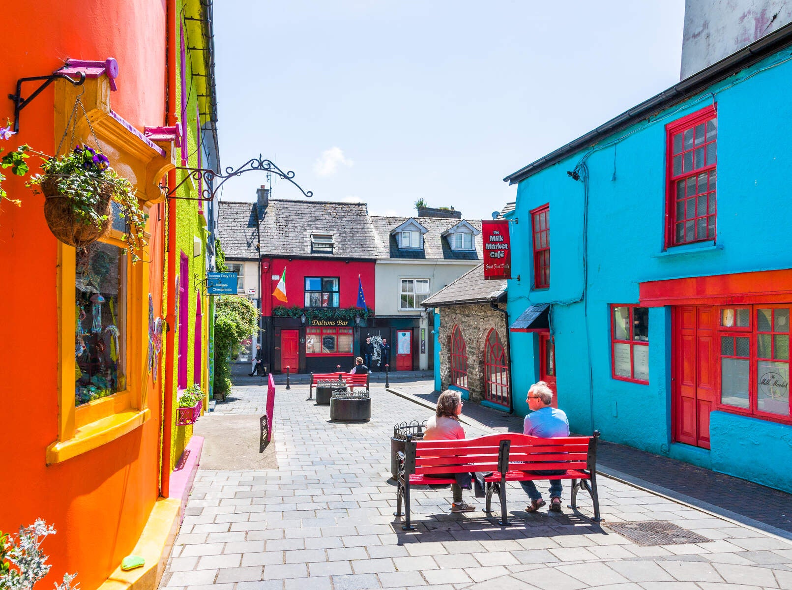 Colourful buildings in Kinsale, Cork with a couple sitting on a red bench.