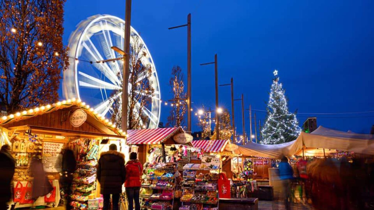 A shot of the Galway Christmas Market with people all around and a Ferris wheel lit up with Christmas lights.