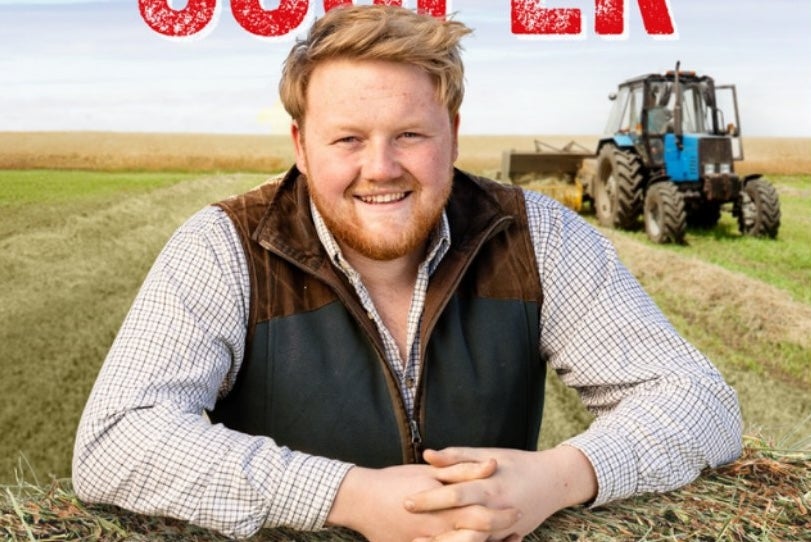 An Evening with Kaleb Cooper, a smiling man resting hands on bale with field behind him