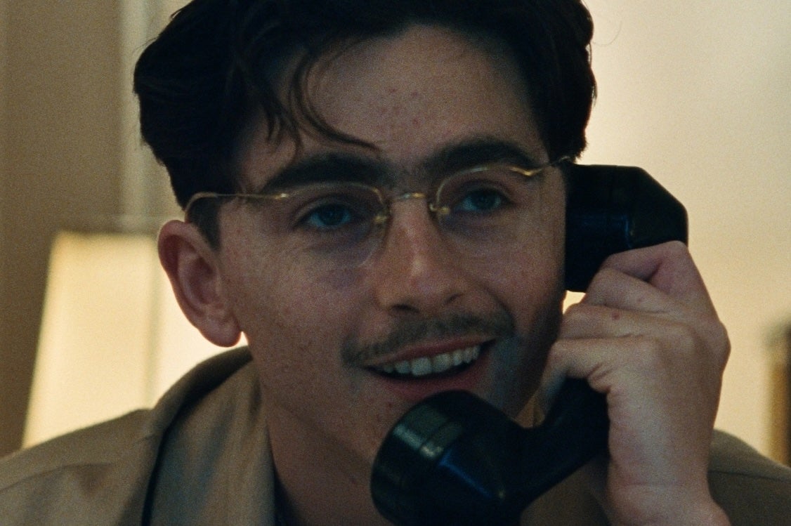 Close up view of man in glasses, smiling talking on an old style telephone.