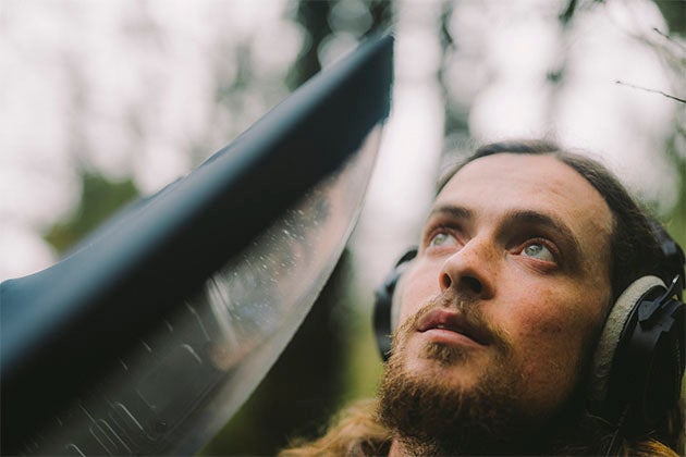 Cork ornithologist Seán Ronayne, a man outdoors wearing overear headphones looking upwards.
