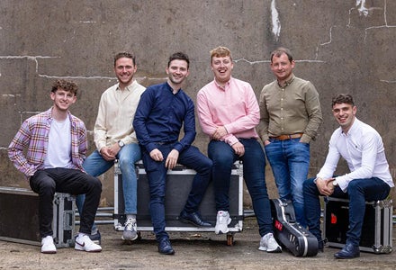 A group of men seated on large black equipment boxes with brown wall behind.