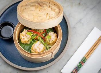 A round bamboo dish with food inside beside chopsticks