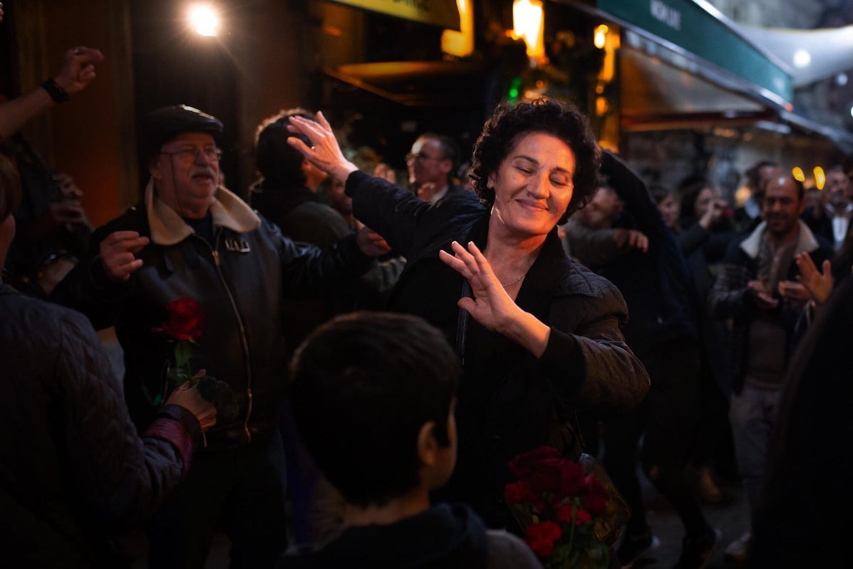 In a crowd at night a woman is dancing, smiling with her eyes closed.