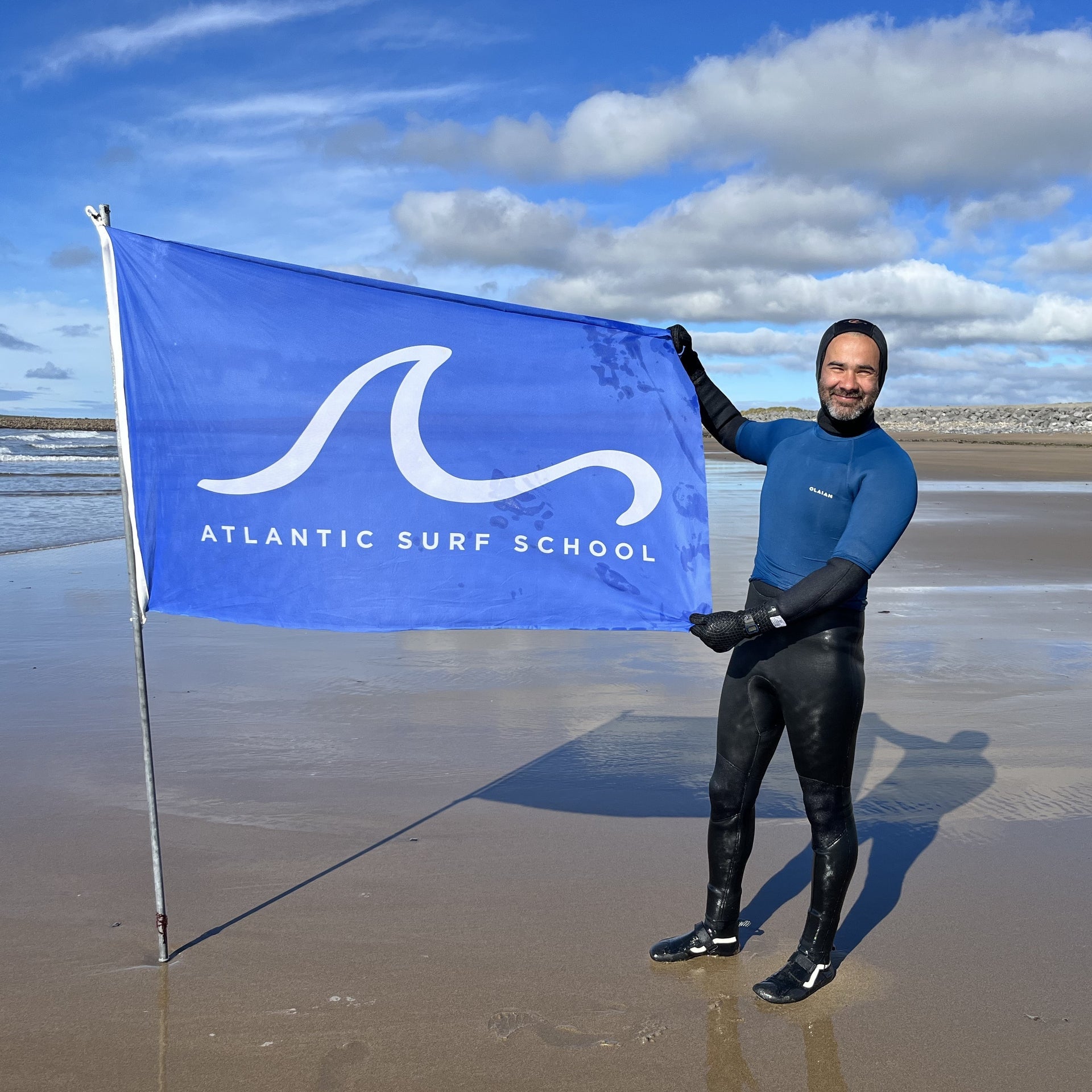Surfer on beach in Strandhill holding Atlantic Surf School flag