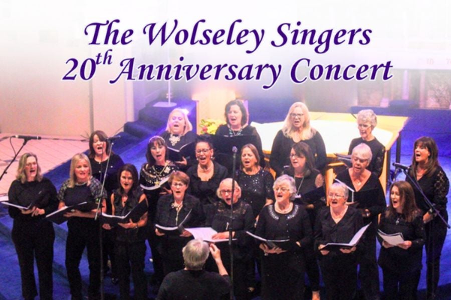 A choir of women holding song sheets, singing with a conductor at the front.