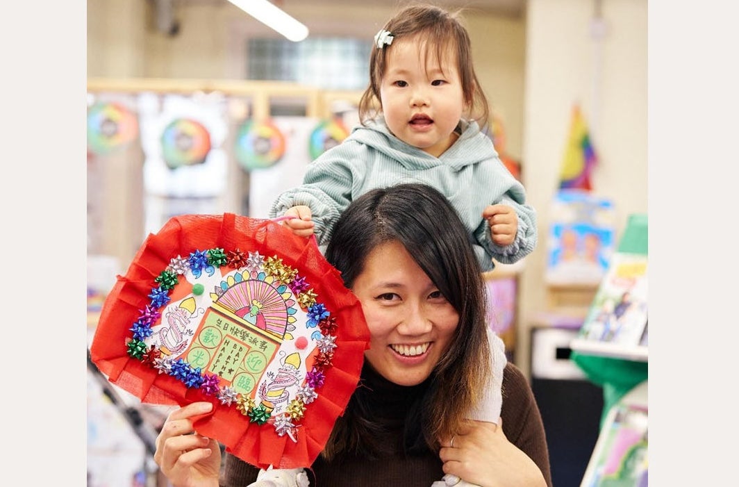 A smiling woman with a small child on her shoulders holding a craft made picture.
