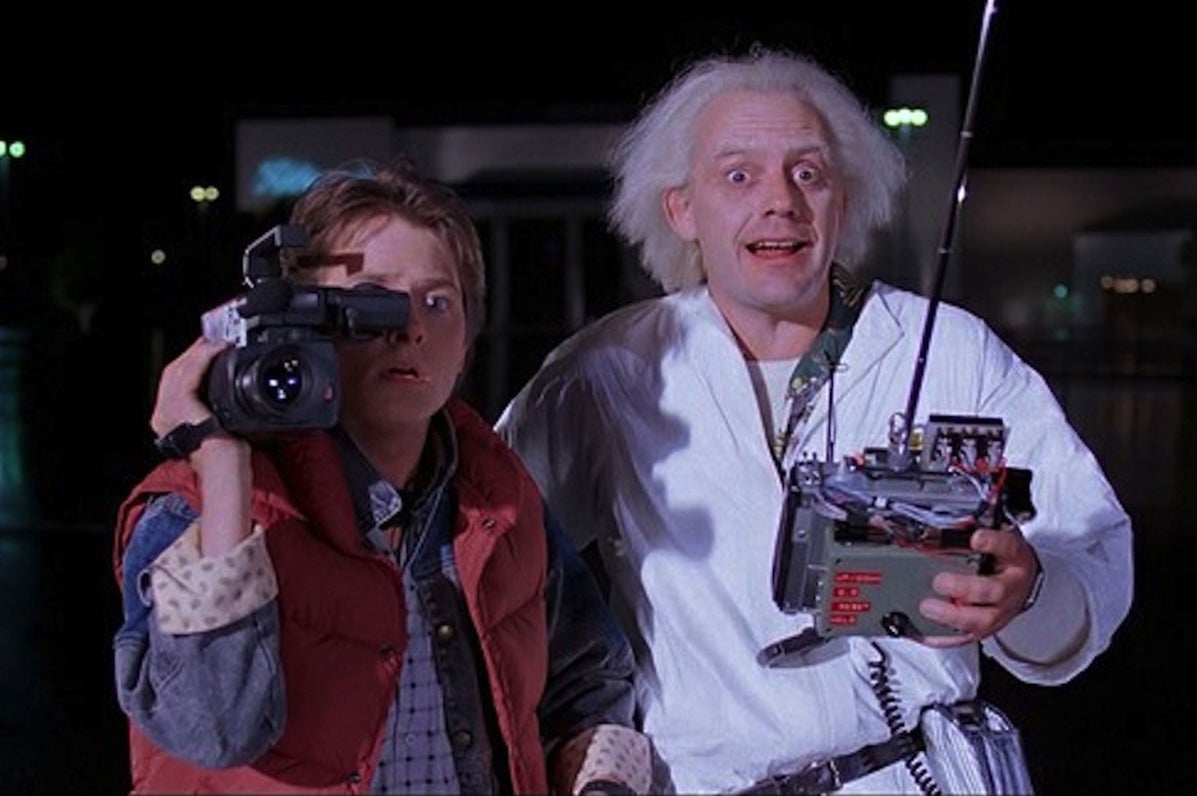 2 shocked looking men, one with a large video camera on one shoulder, the other holding a remote controller.