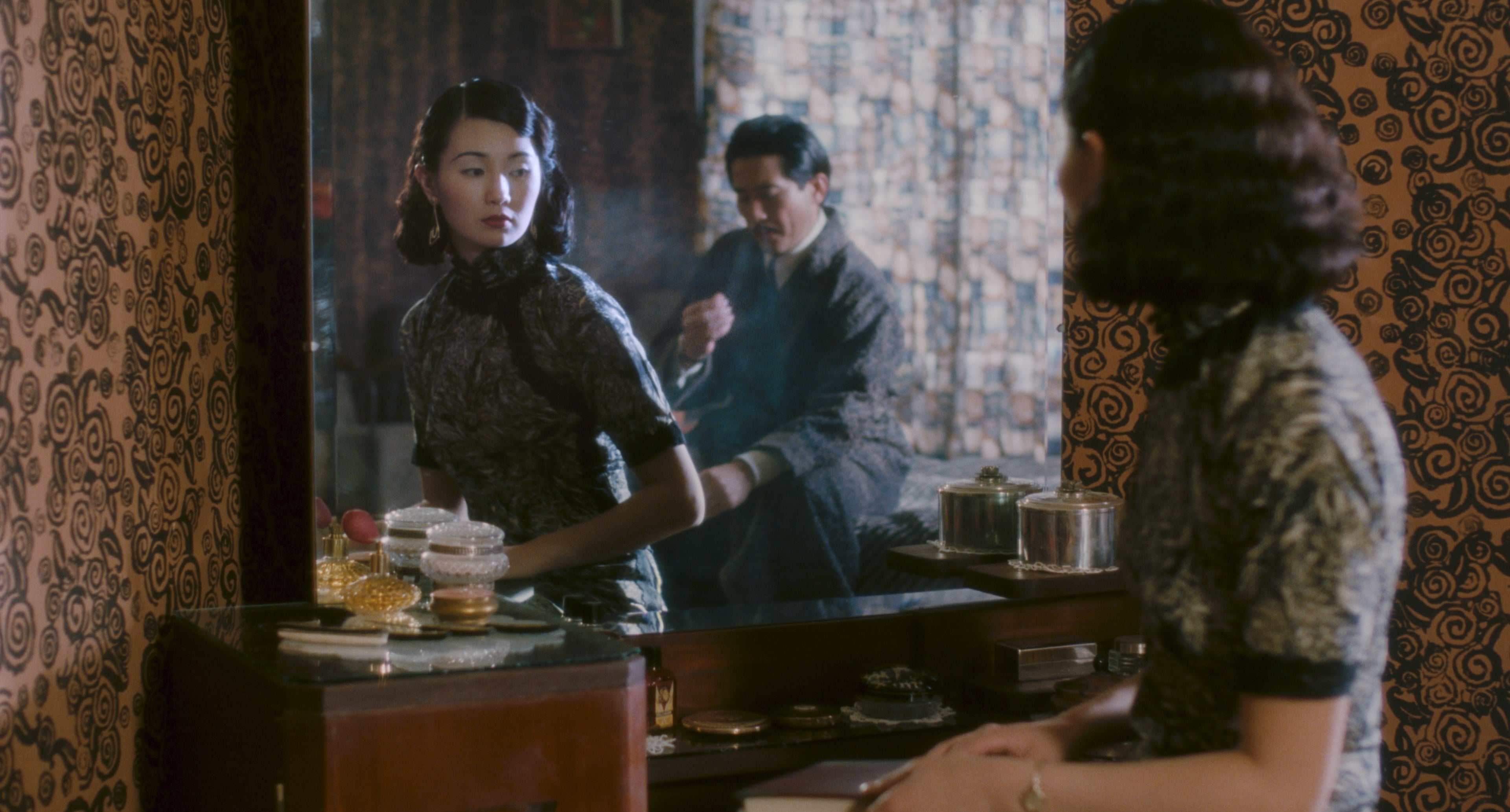 A woman is looking at a mirror. There is a man behind her.