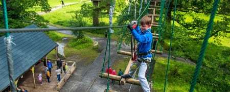 A young boy midway across an open rope and timber bridge