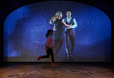 Child dancing in front of a wall with a projected image of two Irish dancers