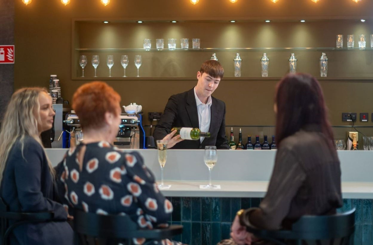 Person serving white wine to three people sitting at the bar