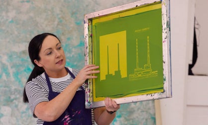 Person wearing a navy apron holding a framed green and yellow print