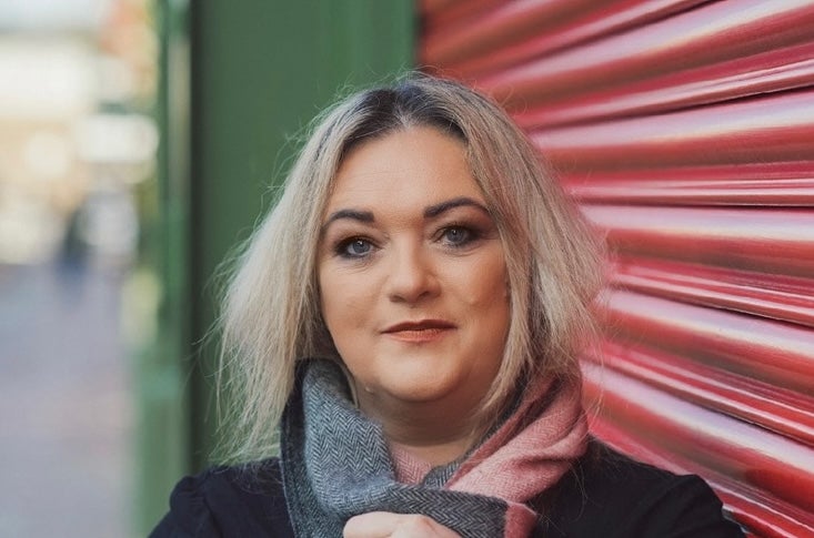 A smiling woman leaning against closed roller blinds over shop window