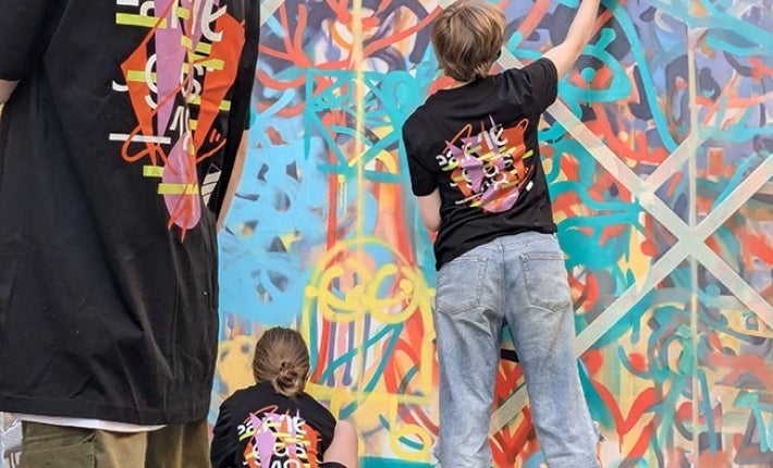 Rear view of youngsters in matching T-shirts working on art on a wall