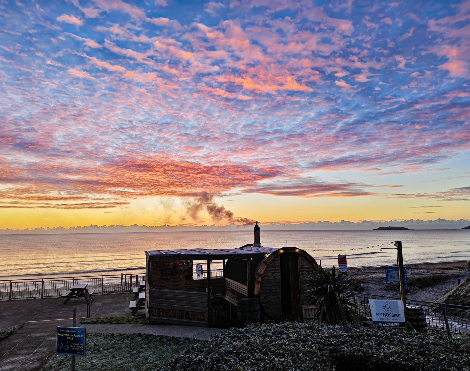 A coastal sauna overlooking a calm sunrise sky filled with pink and orange clouds