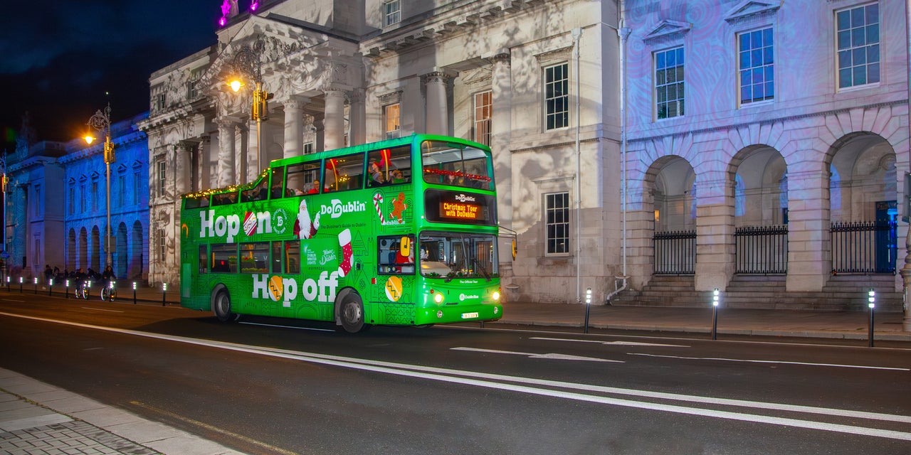 A green double decker bus at night outside old city buildings