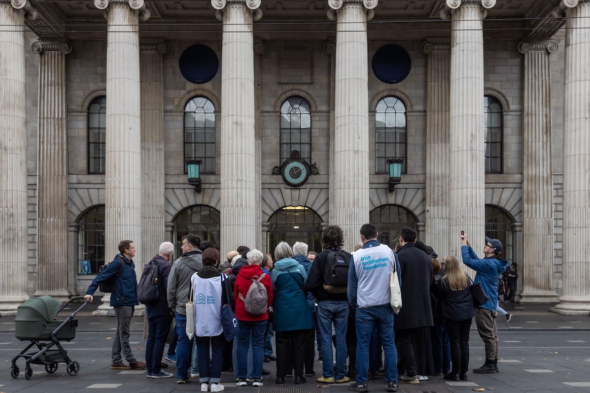 A group of people standing in front of the facade with pillars of grand building.