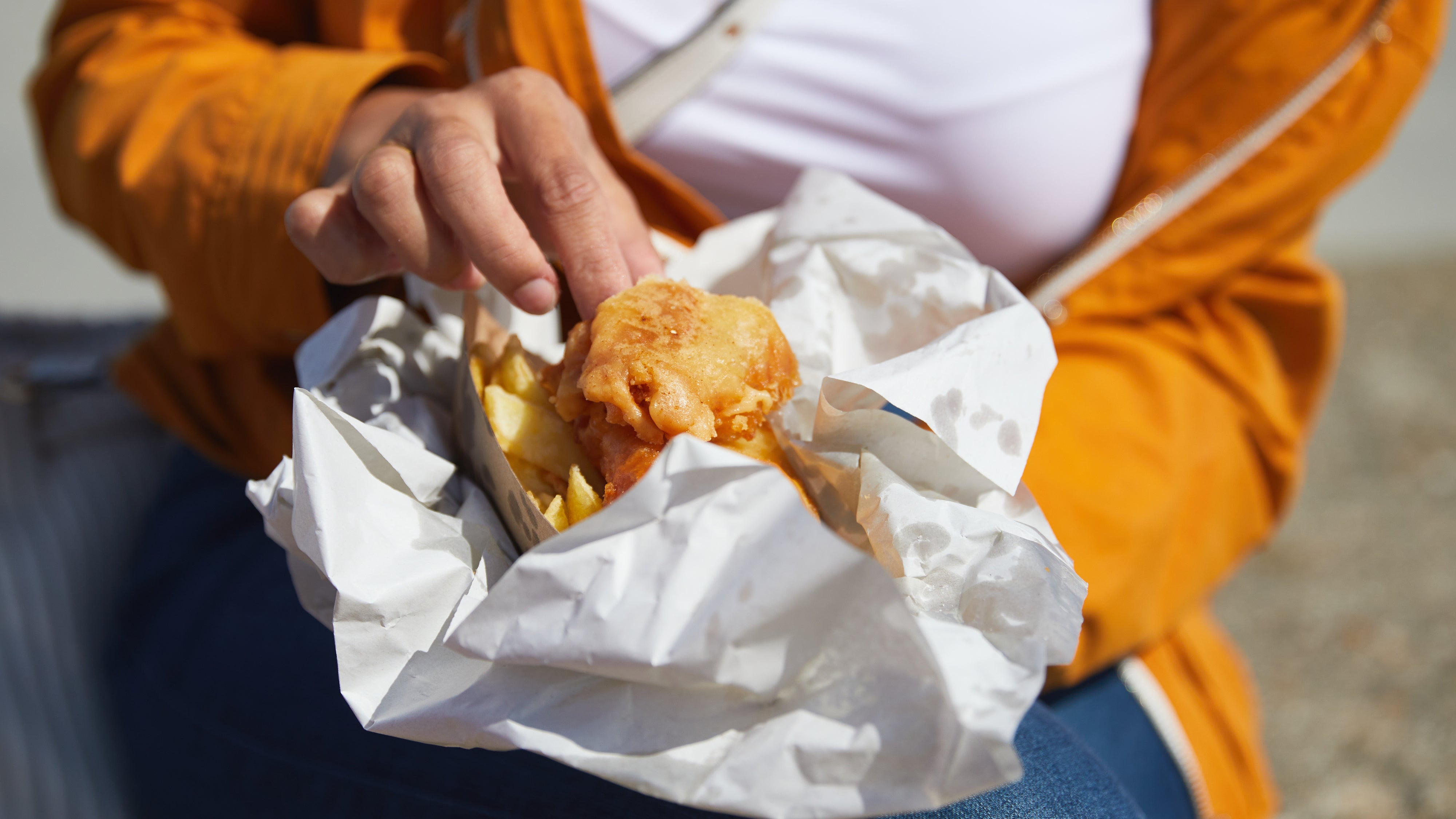 A person holding a portion of fish and chips