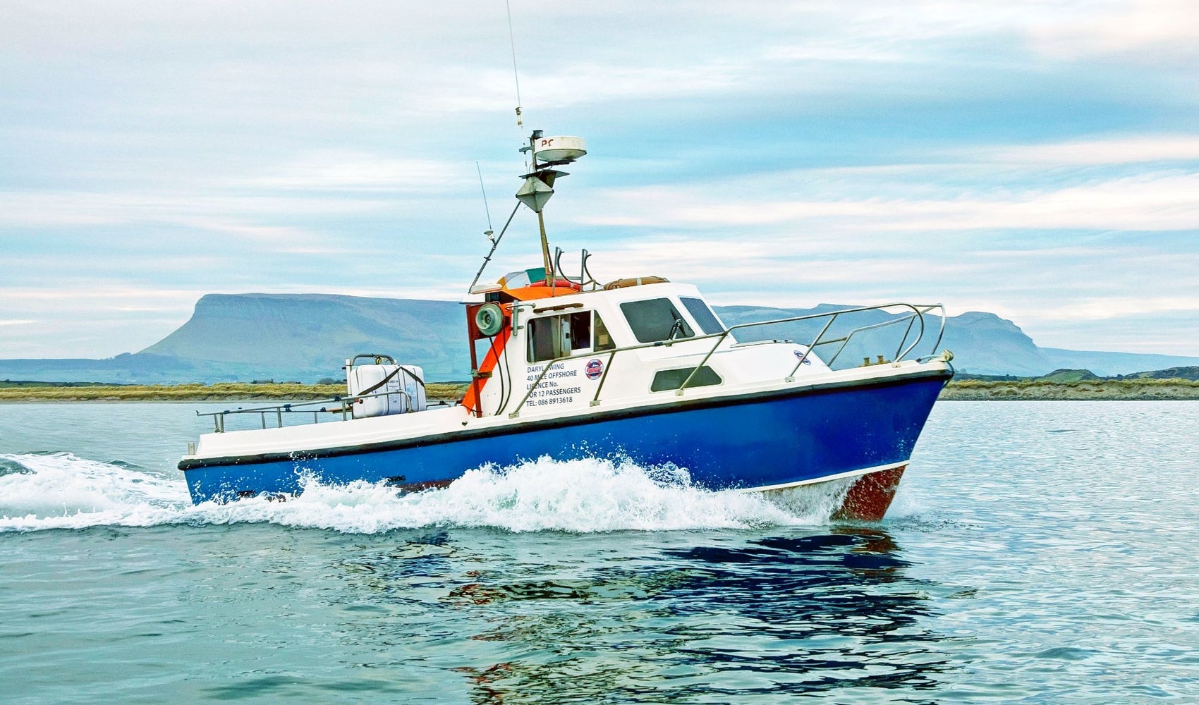 A tour boat speeding through a bay with a mountain in the background